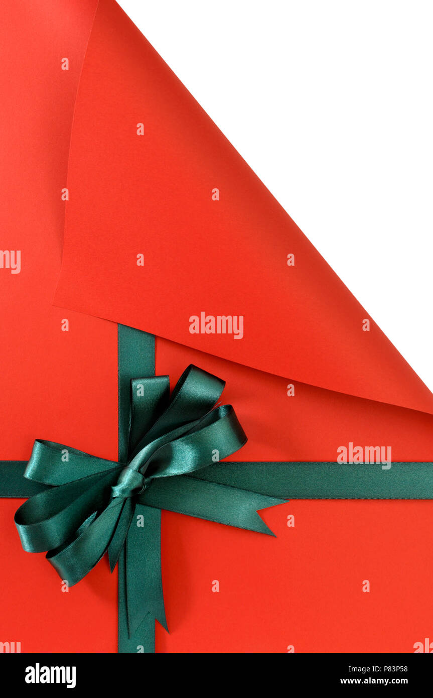 Green gift ribbon bow on plain red background paper, top corner curled open showing white copy space, vertical Stock Photo