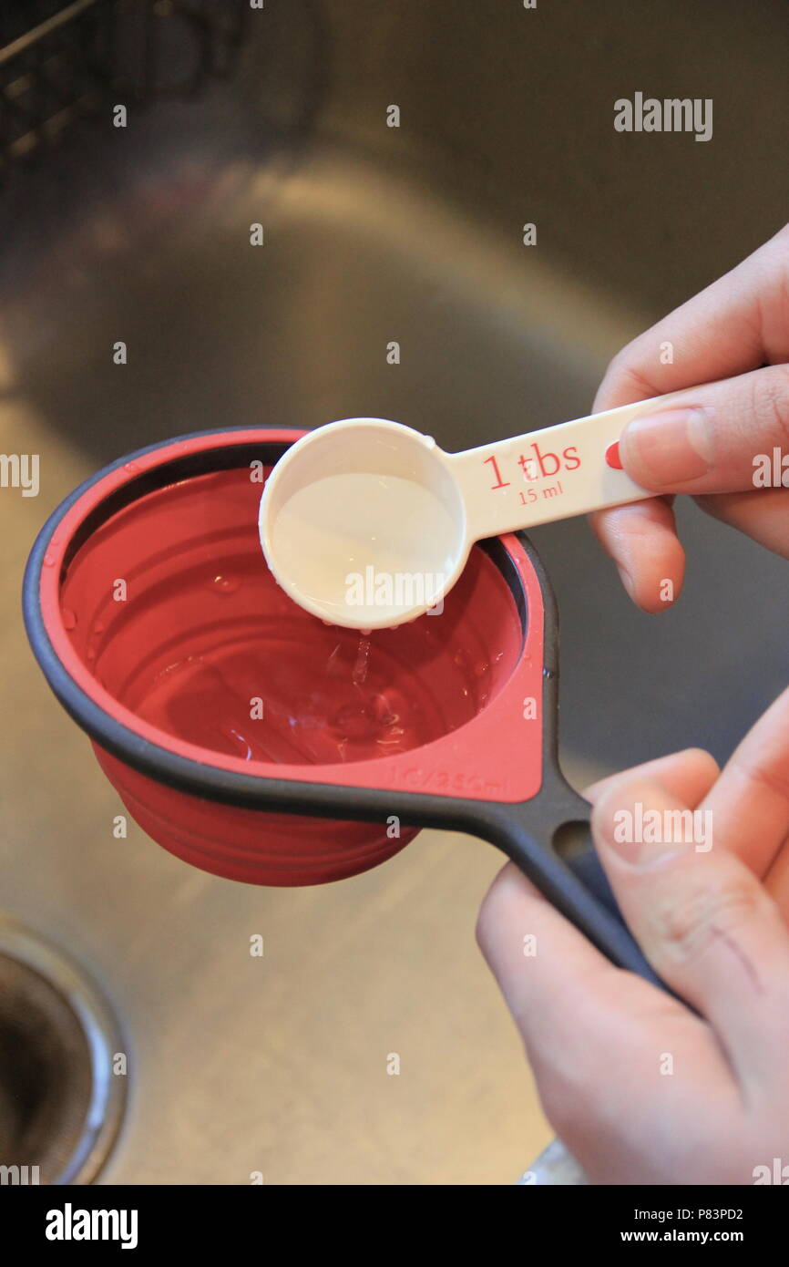 Hand holding tablespoon, pouring water to cup Stock Photo Alamy
