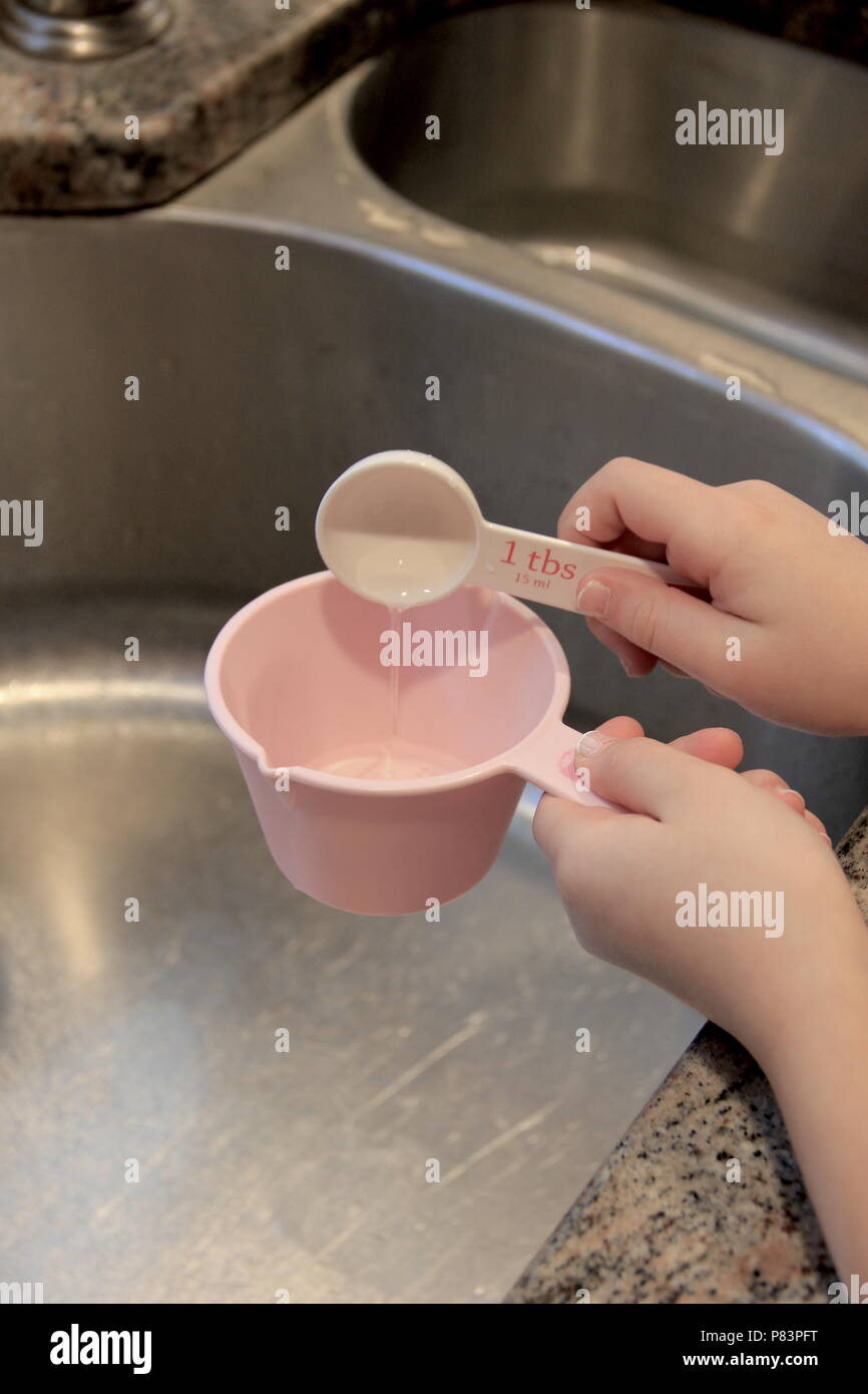 Hand holding tablespoon, pouring water to cup Stock Photo