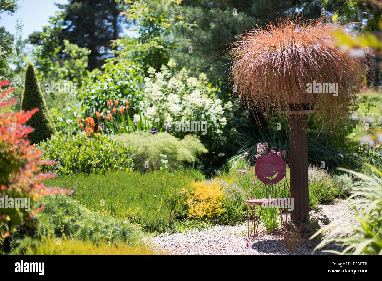 A small metal chair in the shade in a beautiful garden on a sunny day. Stock Photo