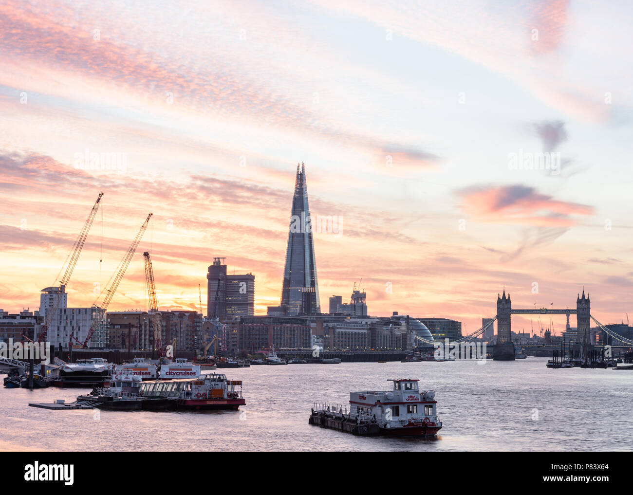Sunset behind The Shard and Tower Bridge in London shot from Bermondsey and with barges and river cruises on the River Thames Stock Photo