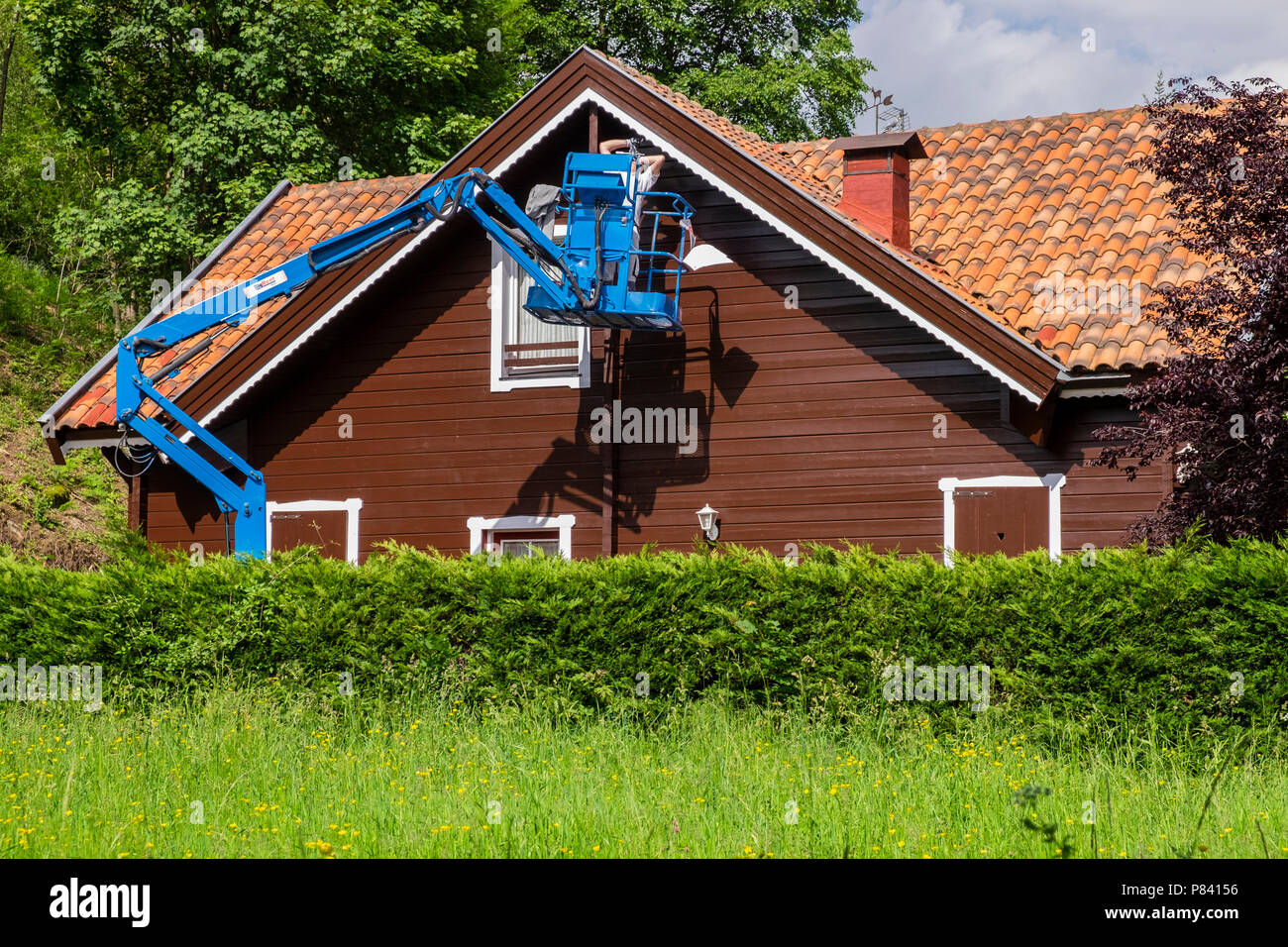 House painter on a scissor lift working under the eaves of a wooden house in Camprodon, Catalonia, Spain Stock Photo