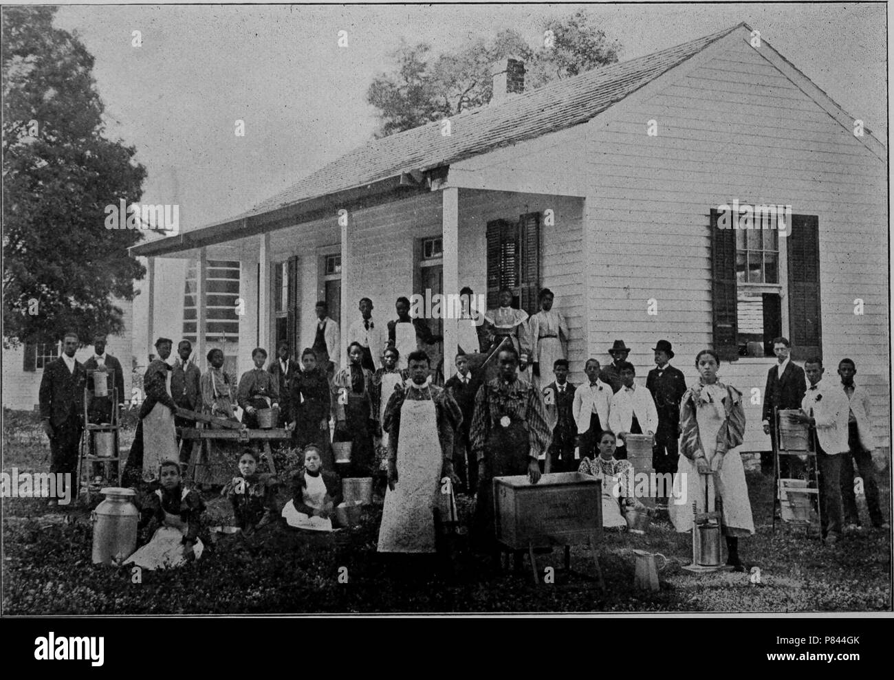 Black and white photograph of Southern University Farm's Dairy Department, comprised by a large group of men and women, some wearing aprons and posing with farm equipment including dairy jugs, with a white, wooden building in the background, located at Southern University in New Orleans, Louisiana, 1893. Courtesy Internet Archive. () Stock Photo