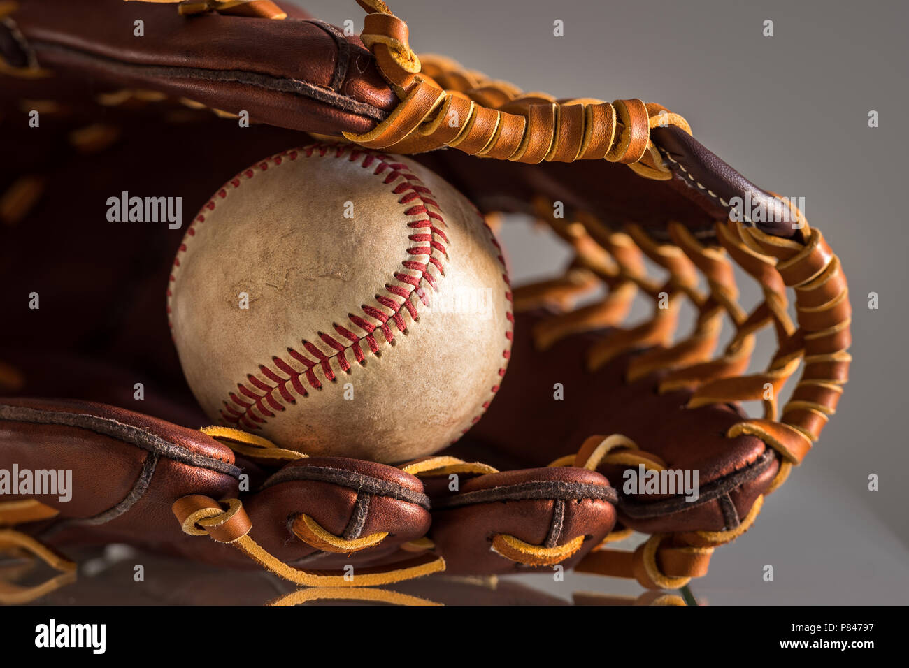 Close-up of a used baseball ball inside brown, leather baseball glove on  plain, grey background Stock Photo - Alamy