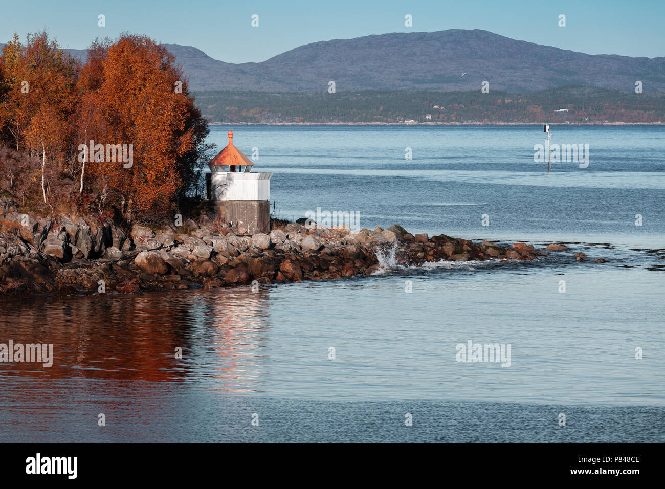 White lighthouse tower with red top on rocky coast of Norwegian Sea ...