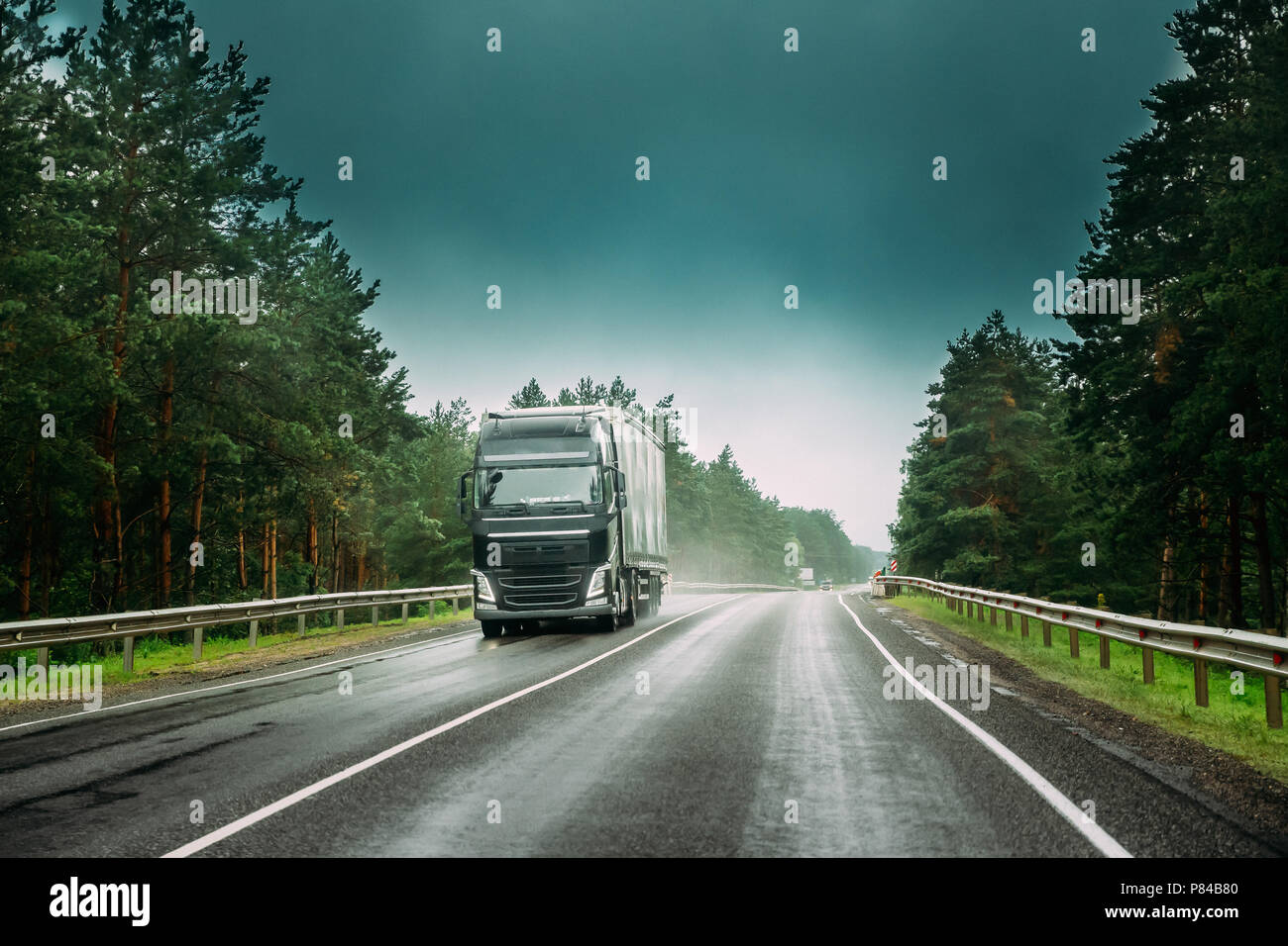 Black Truck Or Tractor Unit, Prime Mover, Traction Unit In Motion On Road, Freeway. Asphalt Motorway Highway Against Background Of Forest Landscape. B Stock Photo