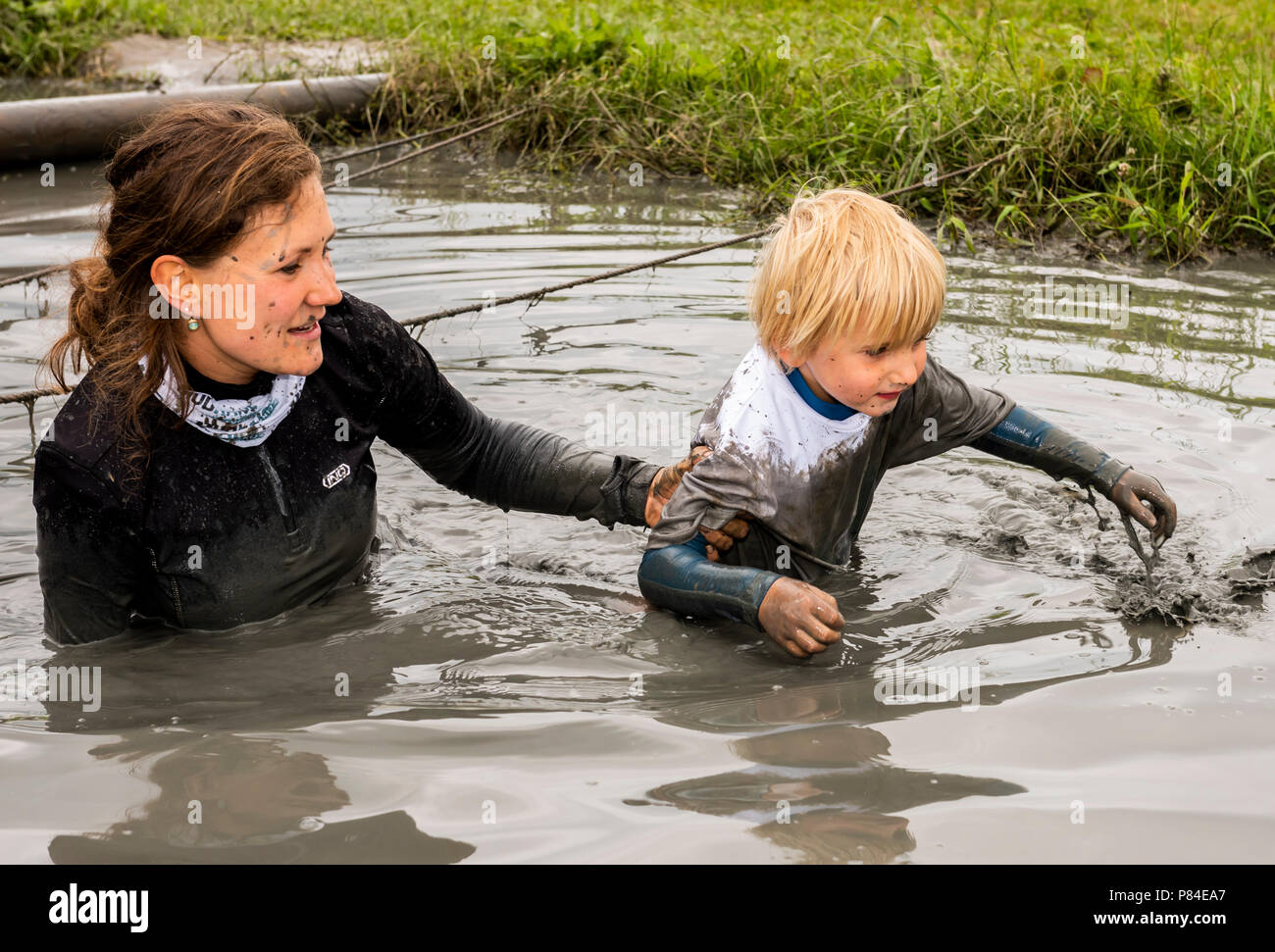 Biddinghuizen, The Netherlands - June 23, 2018: Woman helping child during a mud run (mudraise) in the mud and in the water. Stock Photo