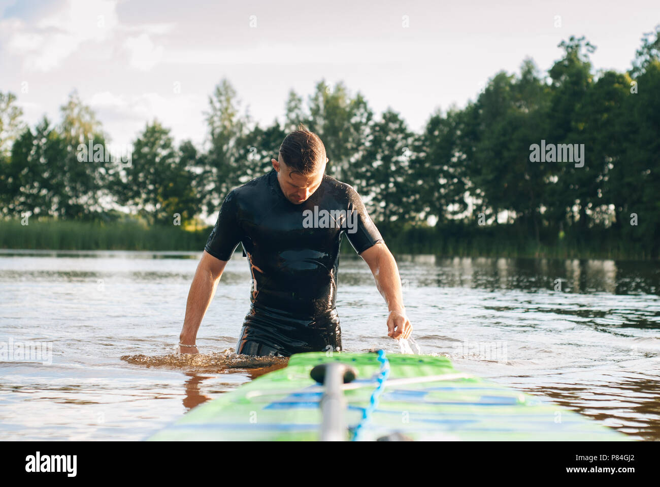 A man in a wetsuit emerges from the water, paddle boarding, SUP Board