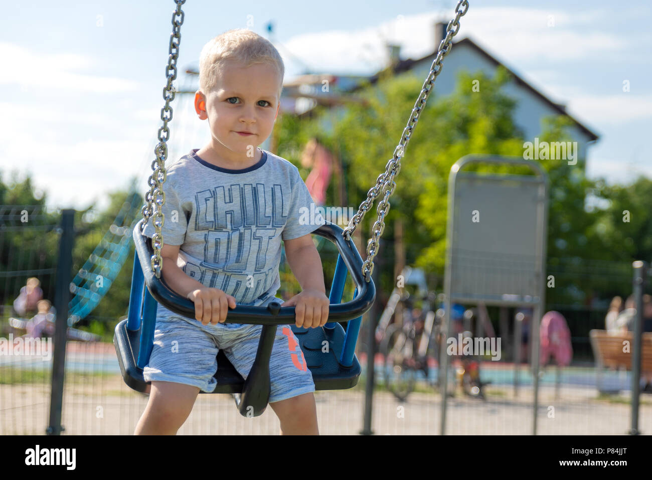 Happy little boy on children playground. Child on a swing. Childhood and leisure concept. Stock Photo