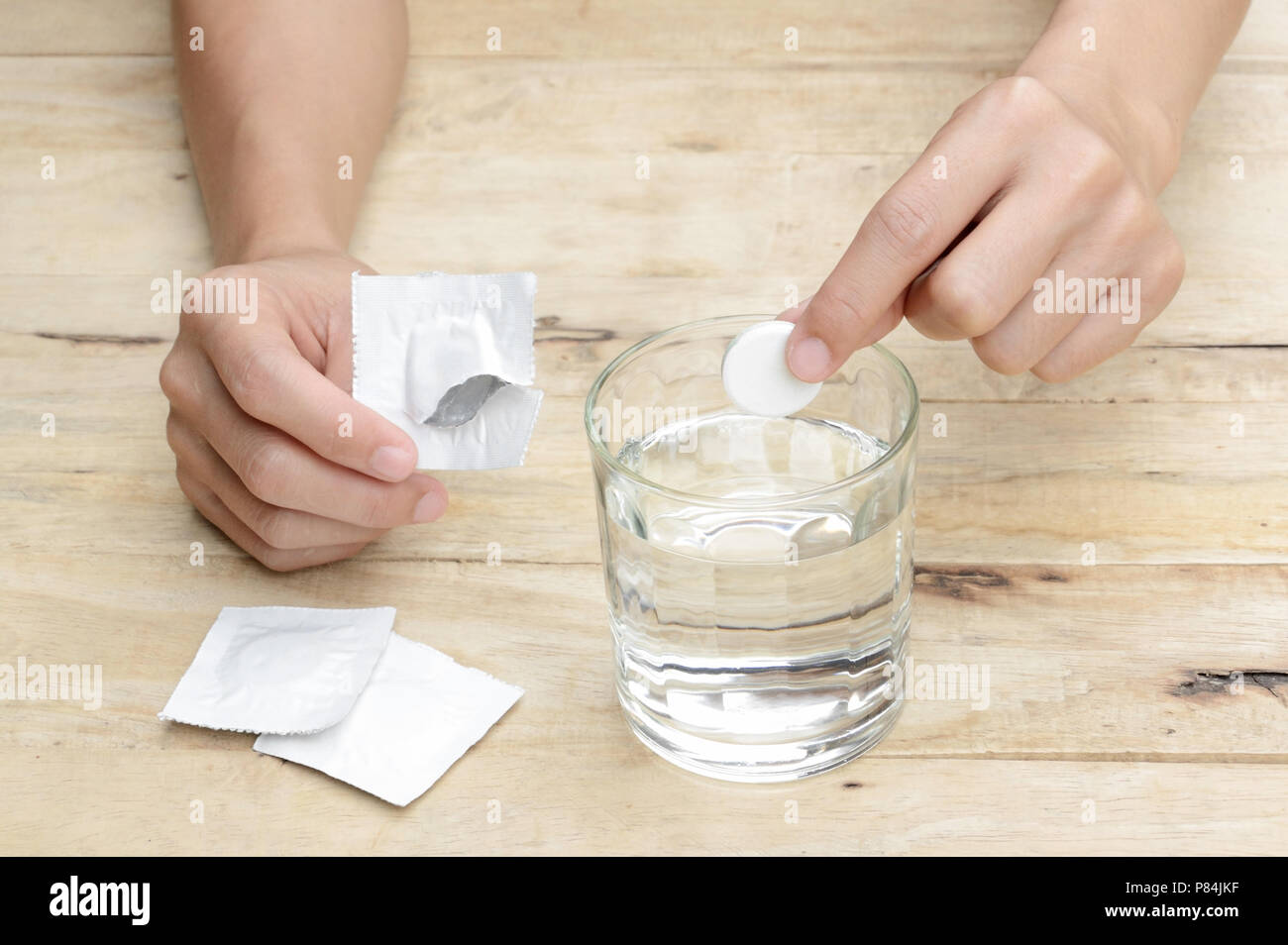 woman hand dropping effervescent tablet in a glass of water on wooden table Stock Photo