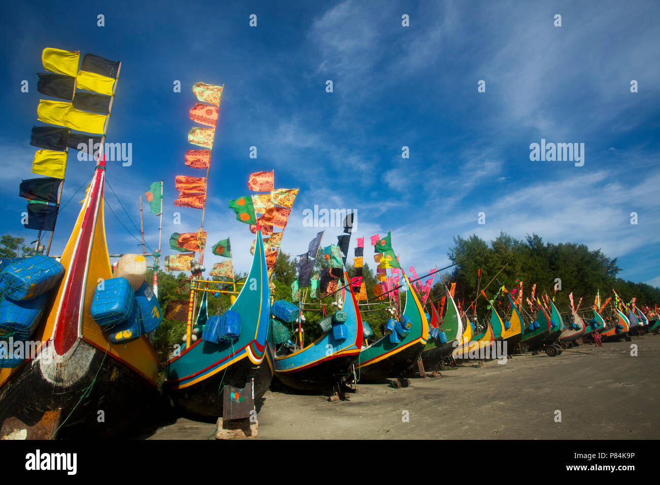 Colourful fishing boats with flags at the Teknaf Sea Beach. It is a part of the Cox's Bazaar Sea Beach, the longest sea beach in the world. Teknaf, Co Stock Photo