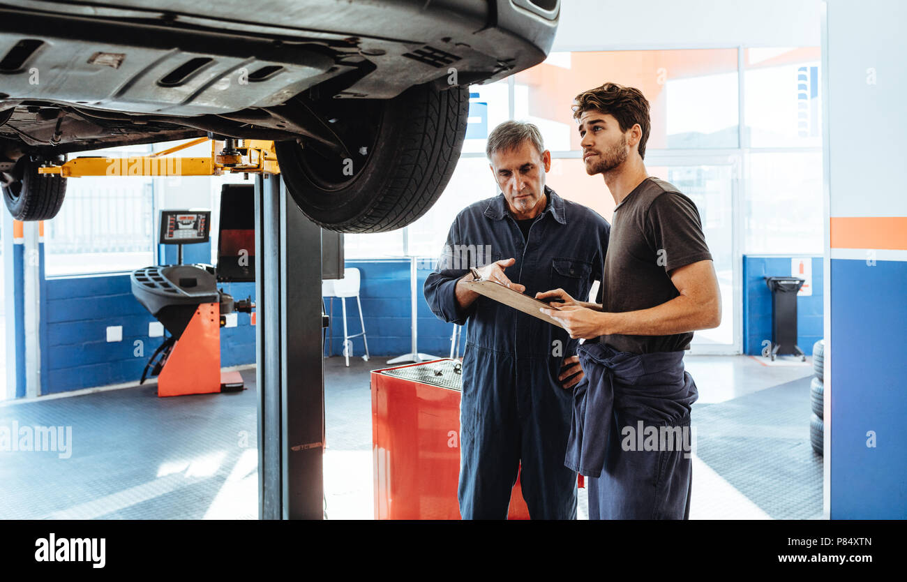 Two car mechanics making a list on clipboard while examining the car