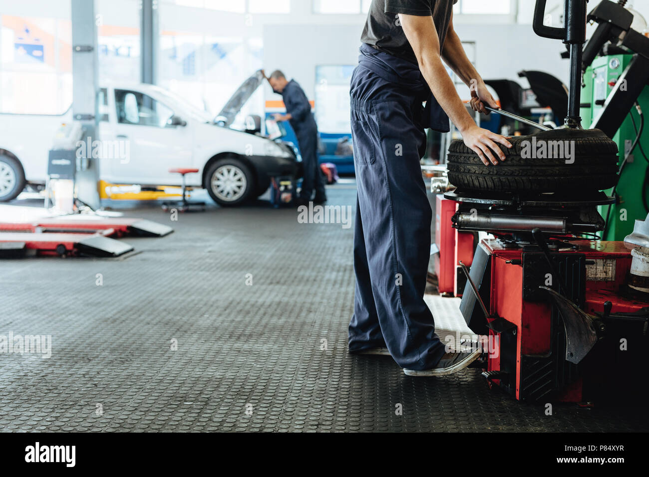 Car repair shop with mechanics working. Mechanic replacing tire of while on machine and other inspecting a vehicle. Stock Photo