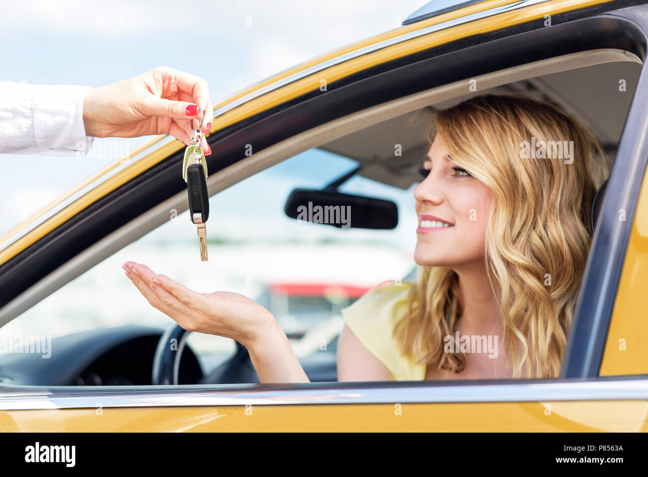 An attractive woman in a car gets the car keys. Rent or purchase of auto. Stock Photo