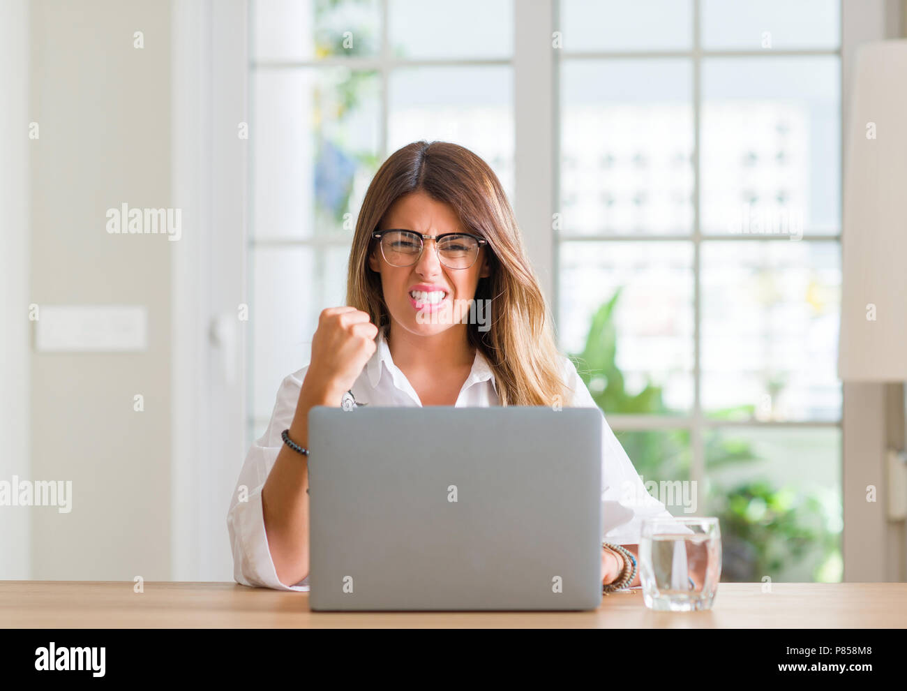 Young woman at home using laptop annoyed and frustrated shouting with ...