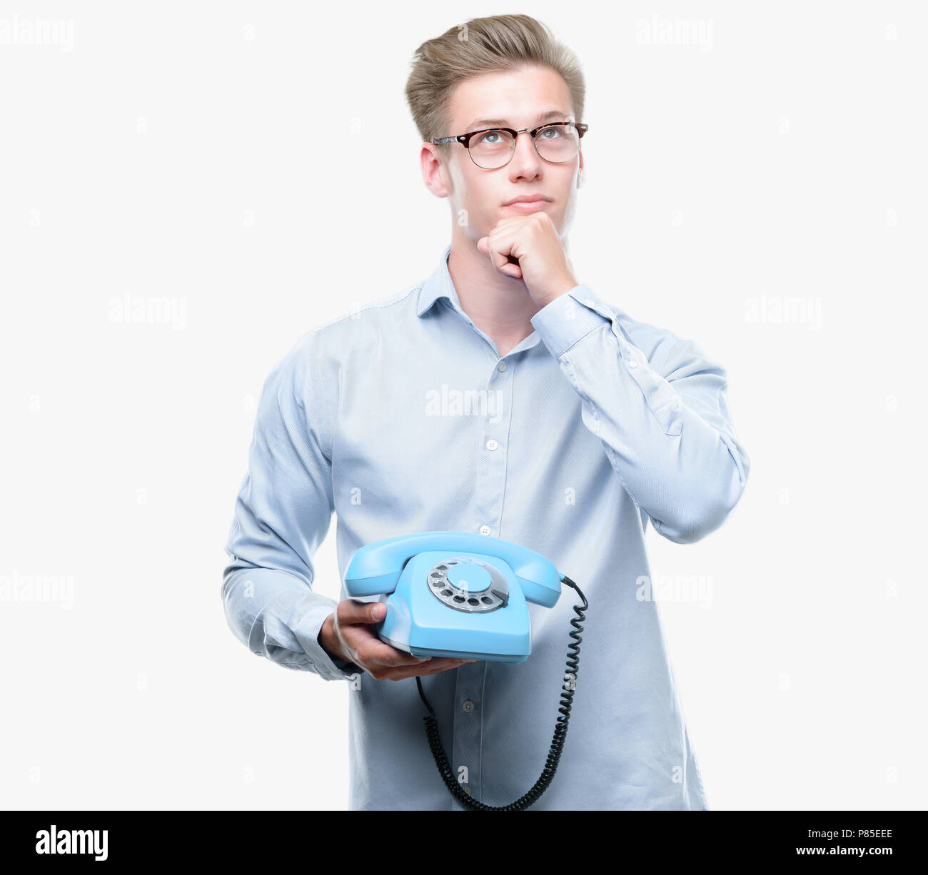 Young handsome blond man holding vintage telephone serious face thinking about question, very confused idea Stock Photo