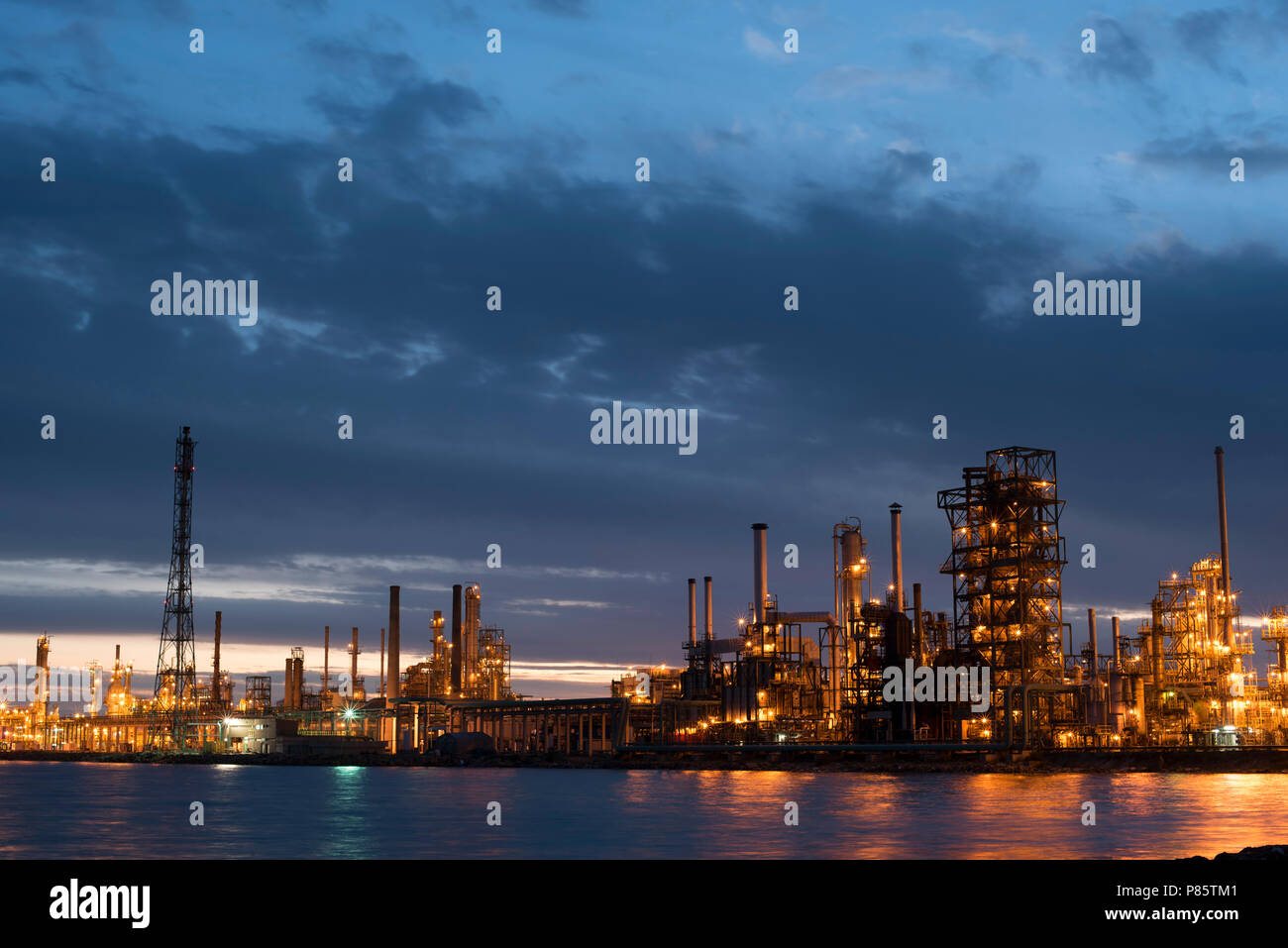Industrial refinery at sunset with cloudy sky, petroleum factory buildings on water coast in dusk time. Stock Photo