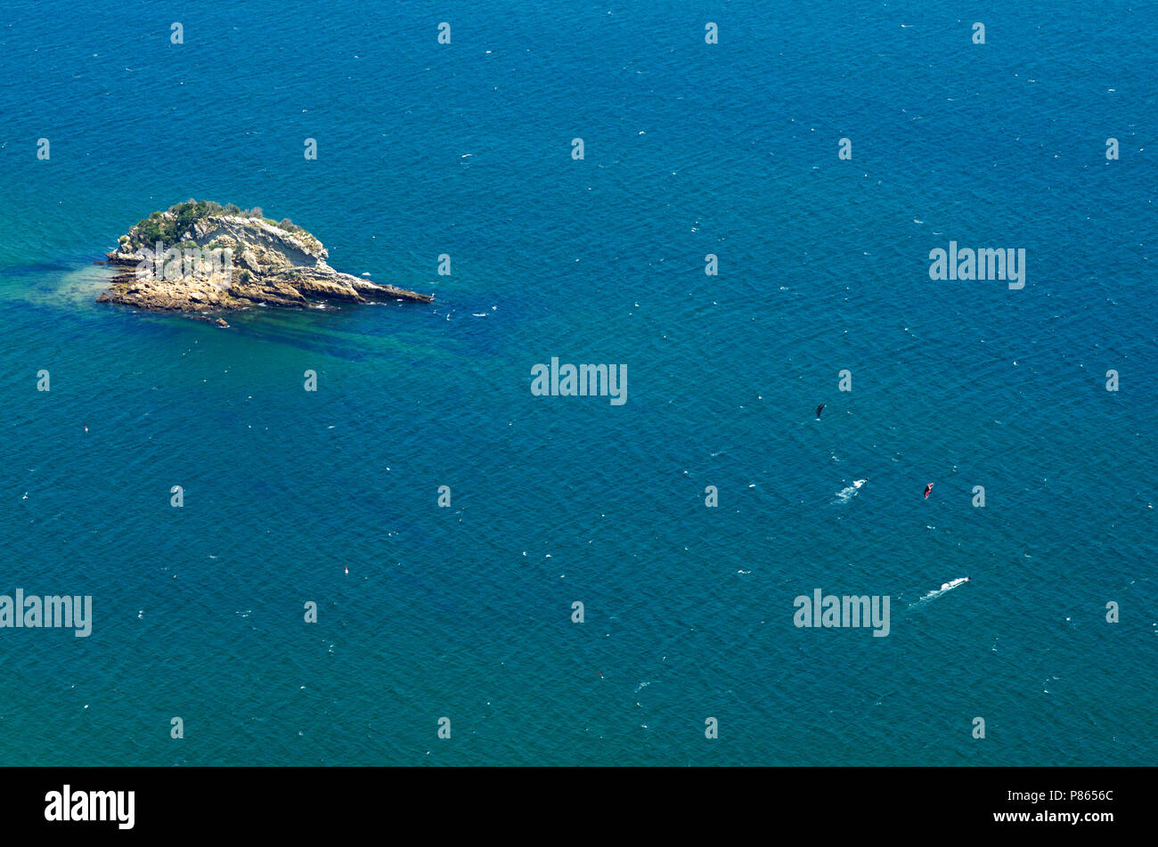 Two kitesurfers, seen from far and above, surfing over blue ocean waters near a small island at Serra da Arrabida beaches. Horizontal composition. Set Stock Photo