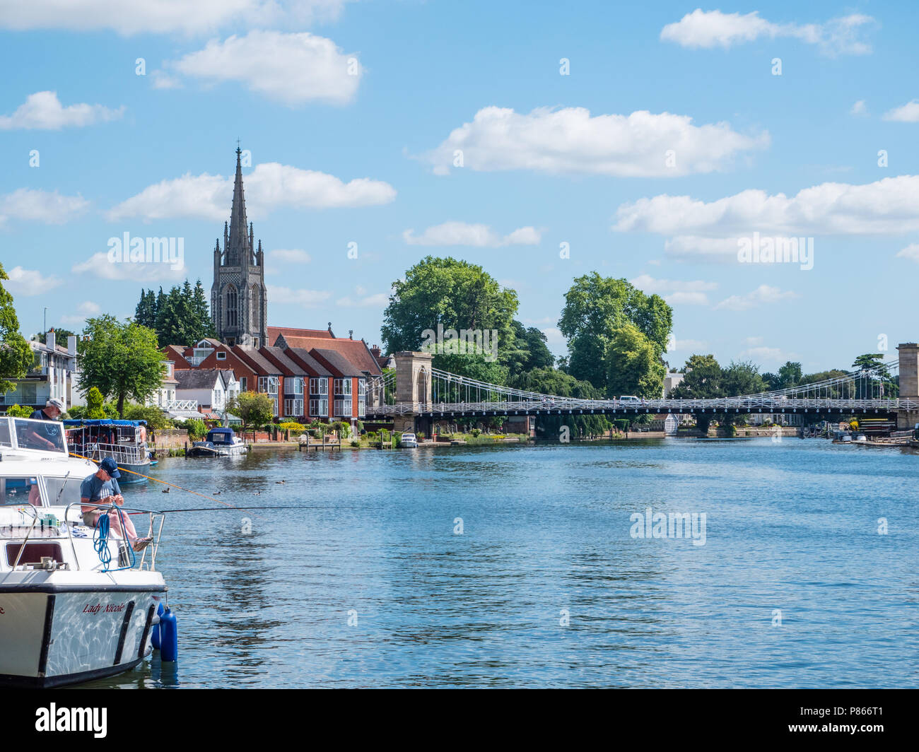 Man Fishing from Boat, with View of River Thames, All Saints Church, Marlow Suspension Bridge, Marlow, Buckinghamshire, England, UK, GB. Stock Photo
