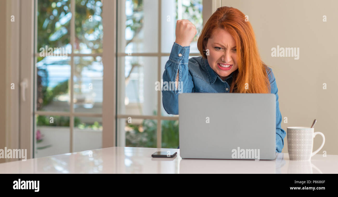 Redhead woman using computer laptop at home annoyed and frustrated ...