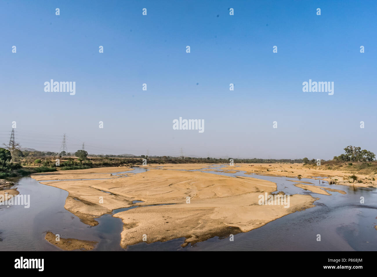 Indian river with clean water in sandy bed  with power grid cable laying background. Stock Photo