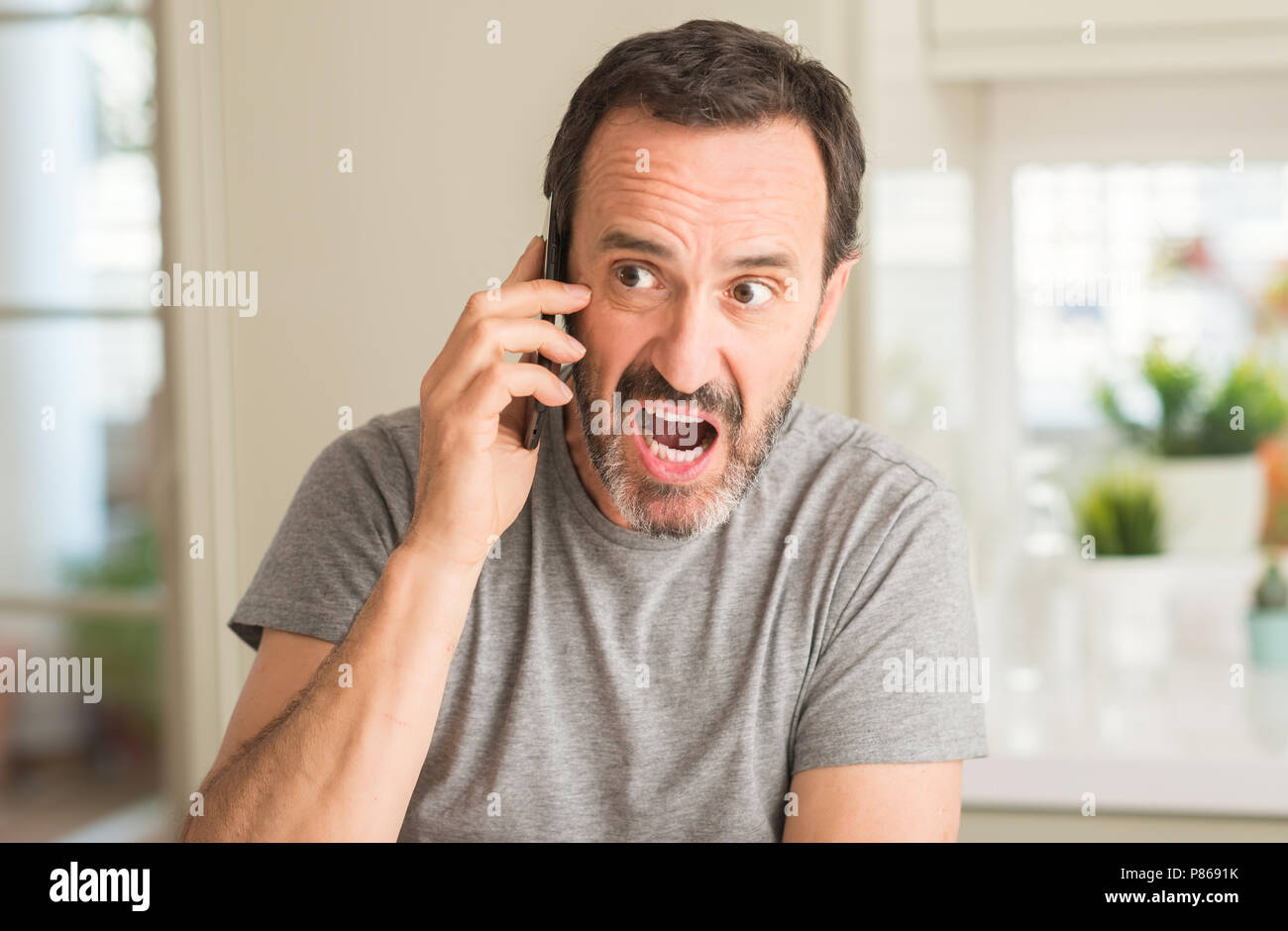 Middle age man using smartphone scared in shock with a surprise face, afraid and excited with fear expression Stock Photo