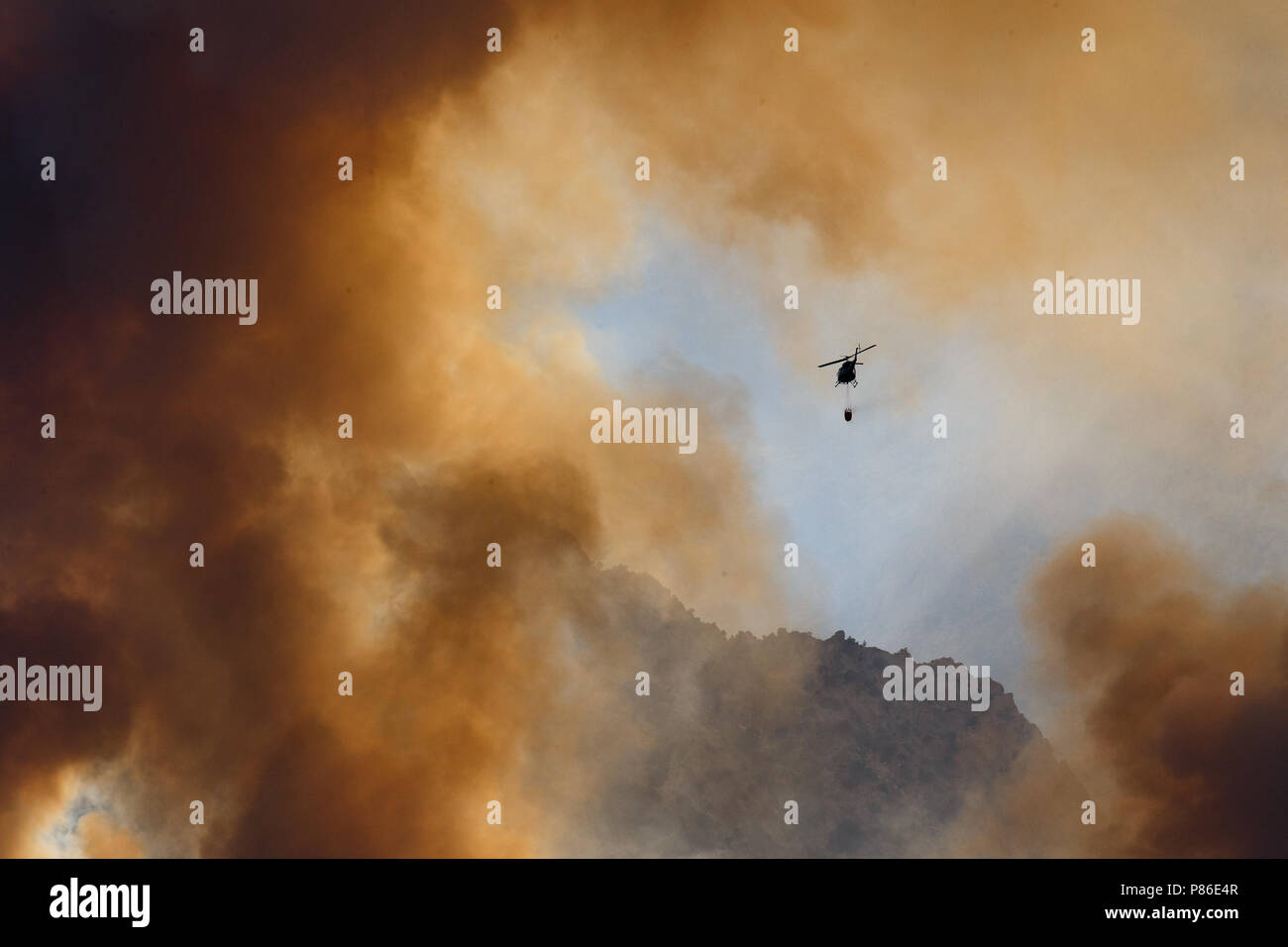 Alabama Hills, Lone Pine, CA. July 8, 2018. A helicopter combats the Georges Fire in the Alabama Hills west of Lone Pine, CA in eastern Sierra Nevadas.  The cause is under investigation. Lightning had been observed in the area. Fire crews from Inyo National Forest, the Bureau of Land Management (BLM),  CALFIRE, and local fire departments are fighting the fire with assistance from air tankers and helicopters. The helicopters are drawing water from the nearby California aquaduct. Stock Photo