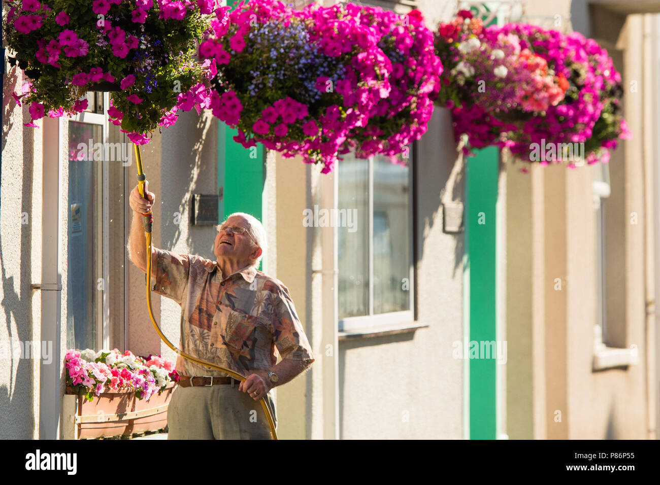 Aberystwyth Wales UK Tuesday 10 July 2018. UK Weather:  A man uses a hosepipe to water the hanging baskets outside his home in Aberystwyth Wales, on yet another hot and sunny morning. The long spell of dry weather continues with  no sign of significant rain in the forecast. Some parts of the UK are experiencing almost drought conditions, with low water levels in many rivers and reservoirs. Hosepipe bans are already in place in Northern Ireland. Photo credit: Keith Morris / Alamy Live News Stock Photo