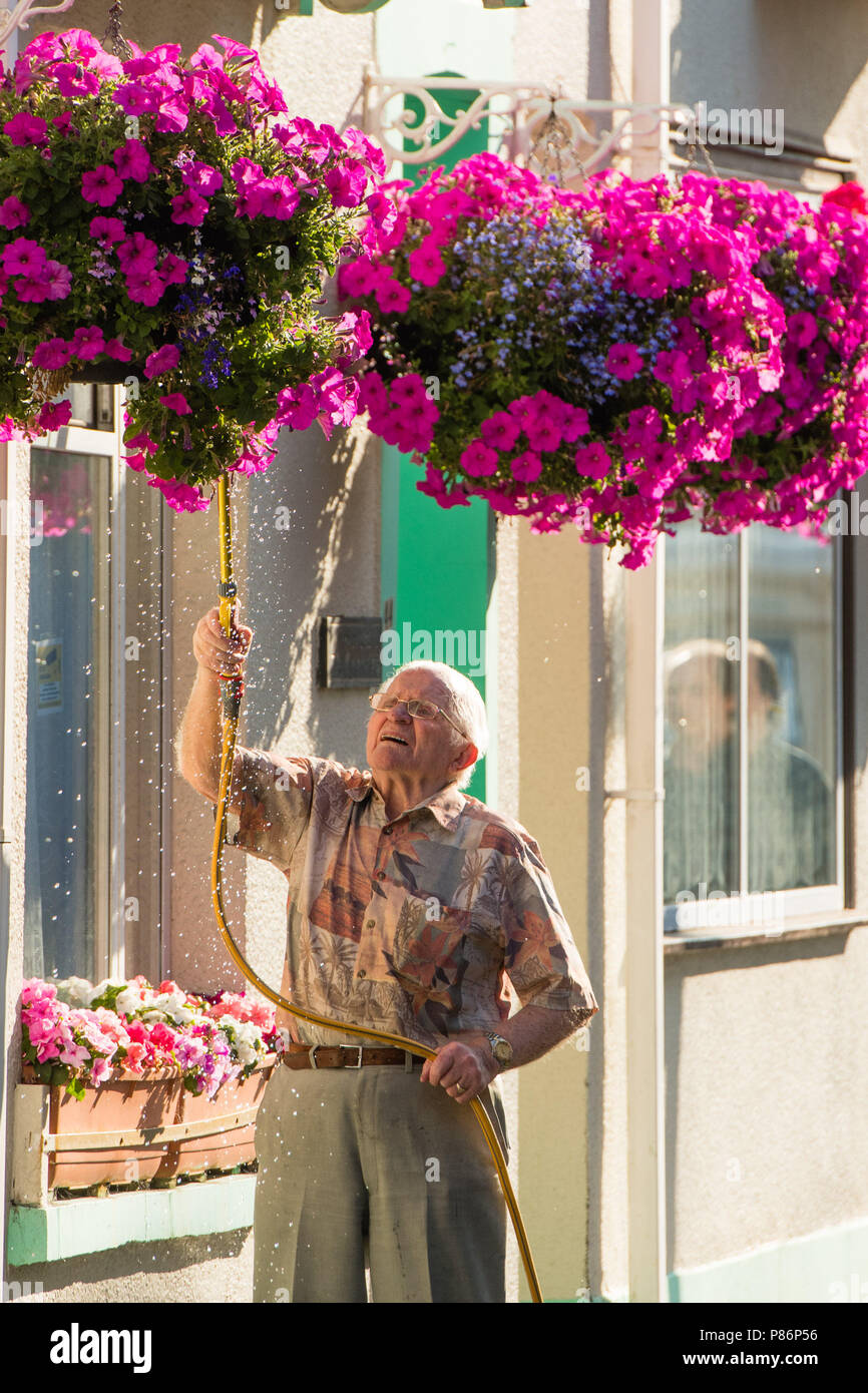 Aberystwyth Wales UK Tuesday 10 July 2018. UK Weather:  A man uses a hosepipe to water the hanging baskets outside his home in Aberystwyth Wales, on yet another hot and sunny morning. The long spell of dry weather continues with  no sign of significant rain in the forecast. Some parts of the UK are experiencing almost drought conditions, with low water levels in many rivers and reservoirs. Hosepipe bans are already in place in Northern Ireland. Photo credit: Keith Morris / Alamy Live News Stock Photo