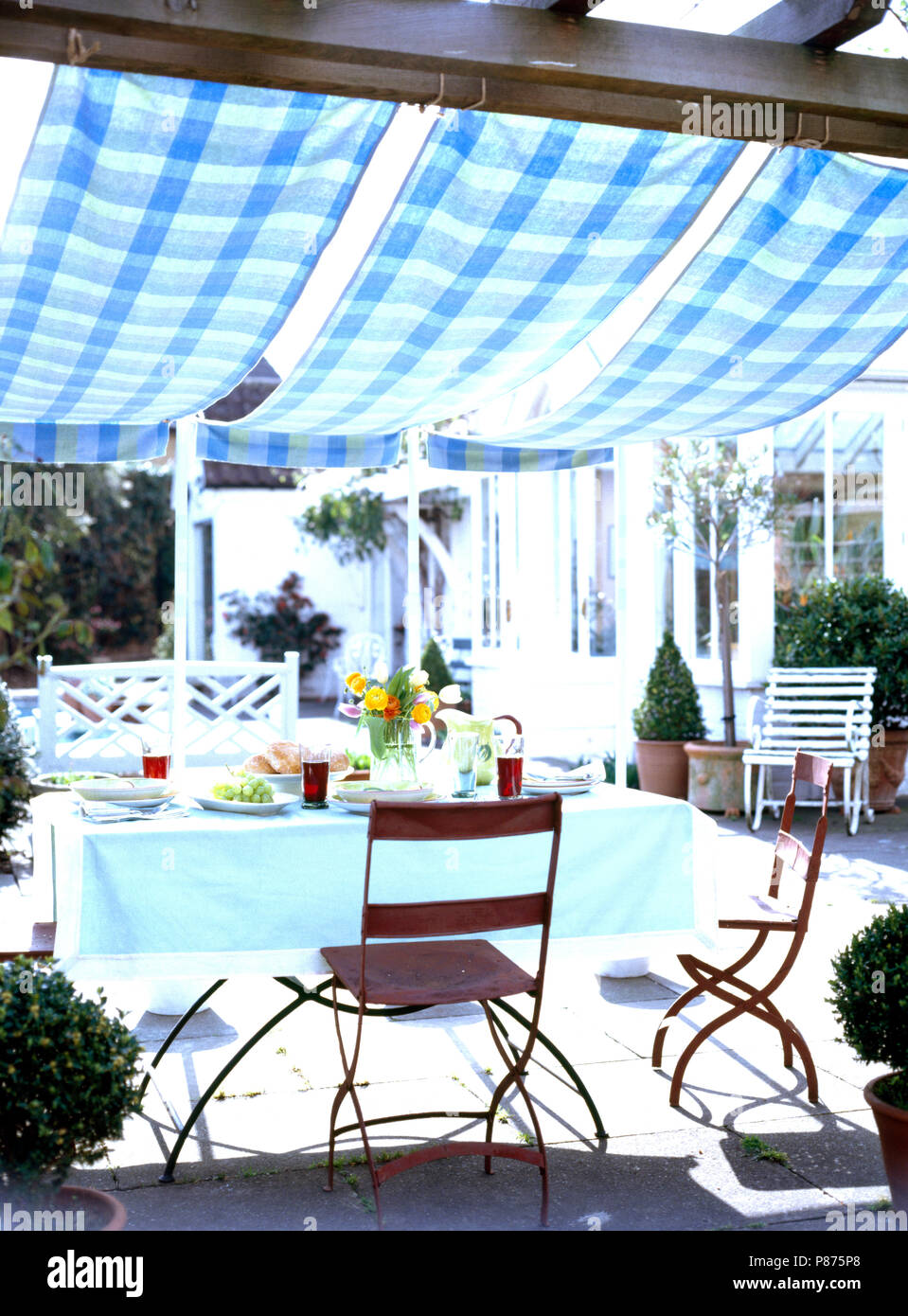 Blue+green checked cotton awning above metal chairs and table set for lunch on the terrace Stock Photo