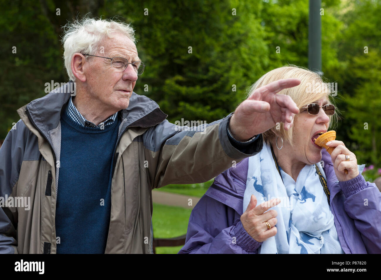 Woman eats an ice-cream while being given directions, Pavilion Gardens, Buxton, Derbyshire, England, UK Stock Photo