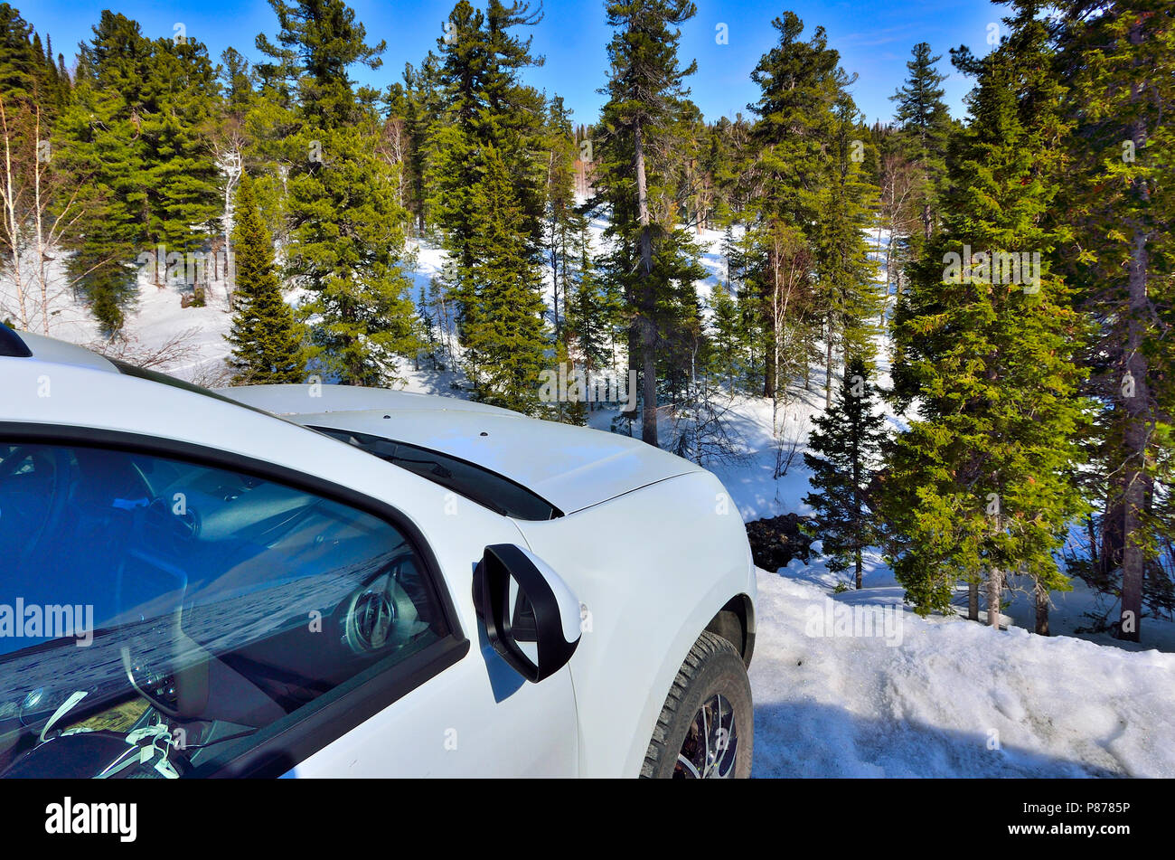 Side view of white car on the edge of cliff in winter mountain landscape over snowy coniferous forest  at sunny day - concept of a reliable vehicle fo Stock Photo