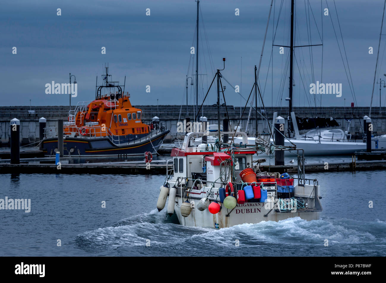 Fishing boat leaving Dun Laoghaire habour with RNLI lifeboat Stock Photo
