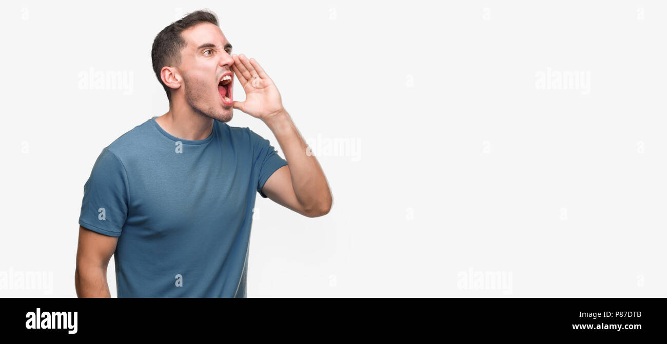 Handsome young casual man shouting and screaming loud to side with hand ...