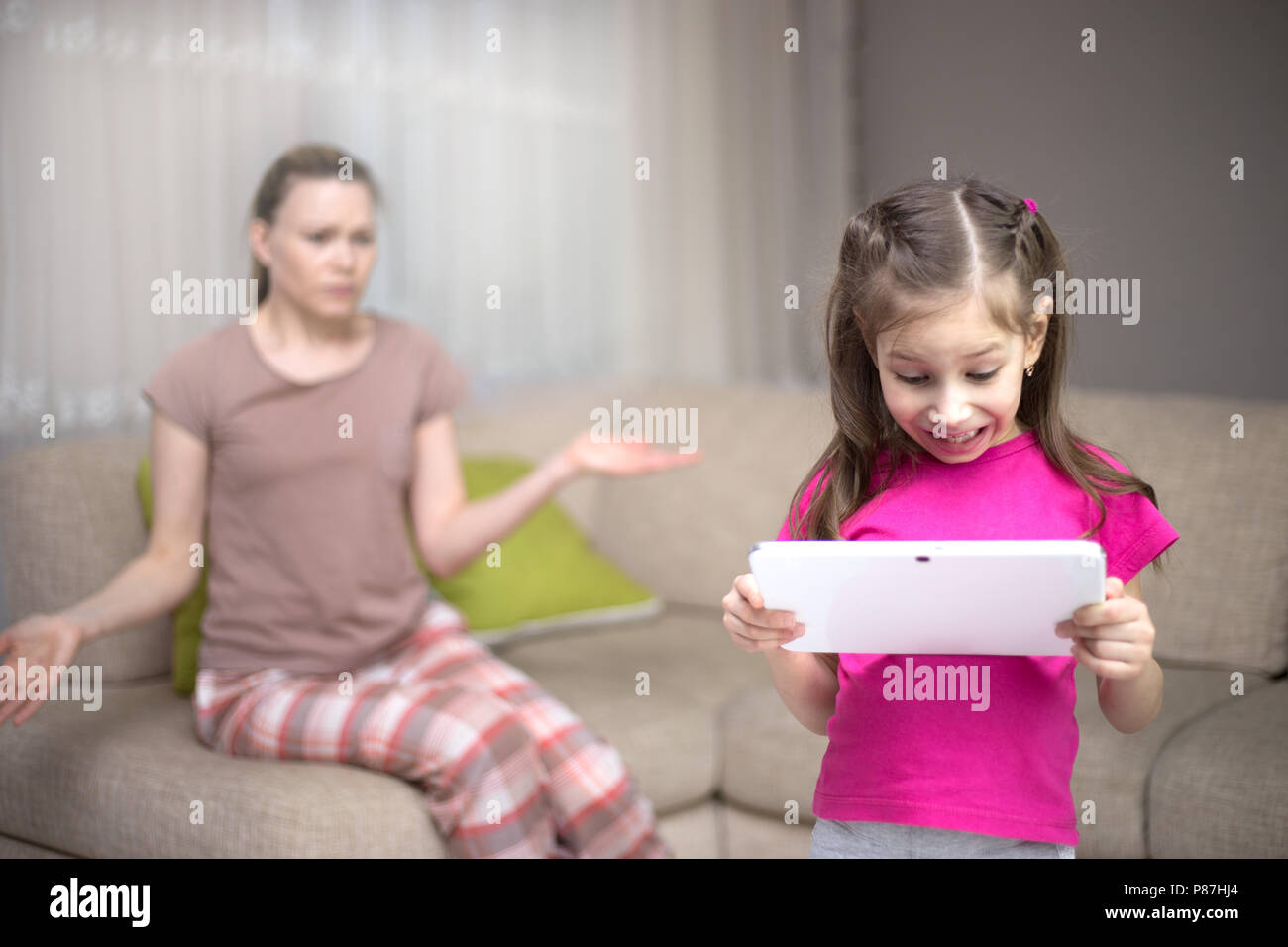 Mother frustrating that her daughter playing video games. Happy child girl and sad mother. Stock Photo