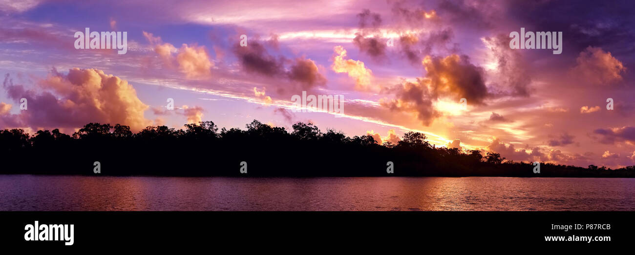 A striking inspirational Red/Pink colored cloudy sunrise  seascape over sea water with water reflections.  Captured in Queensland , Australia. Stock Photo