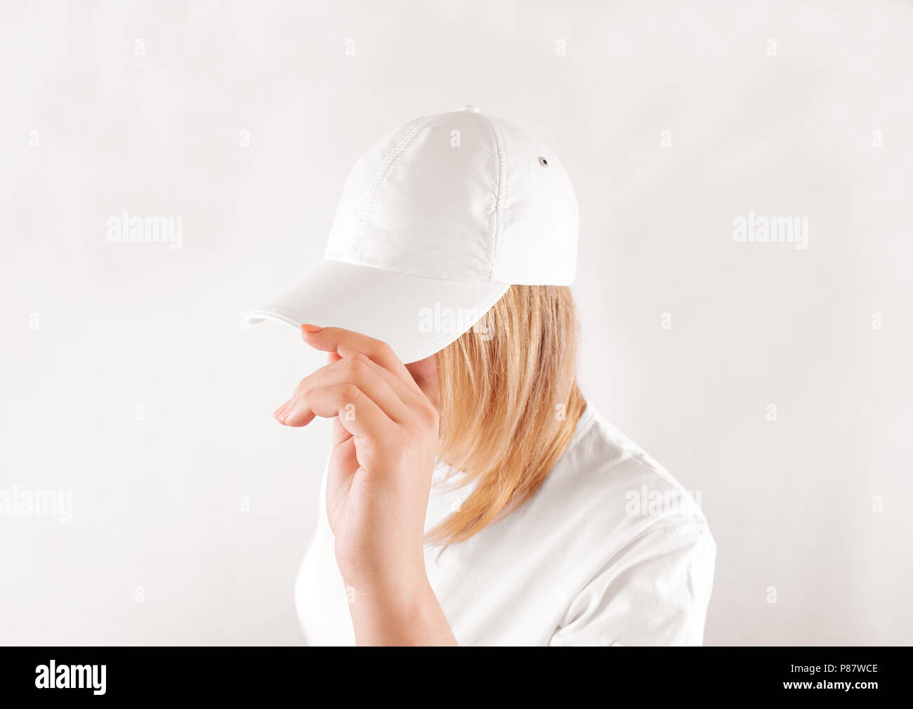 Blank white baseball cap mockup template, wear on women head, isolated, side view. Woman in clear hat and t shirt uniform mock up holding visor of cap Stock Photo