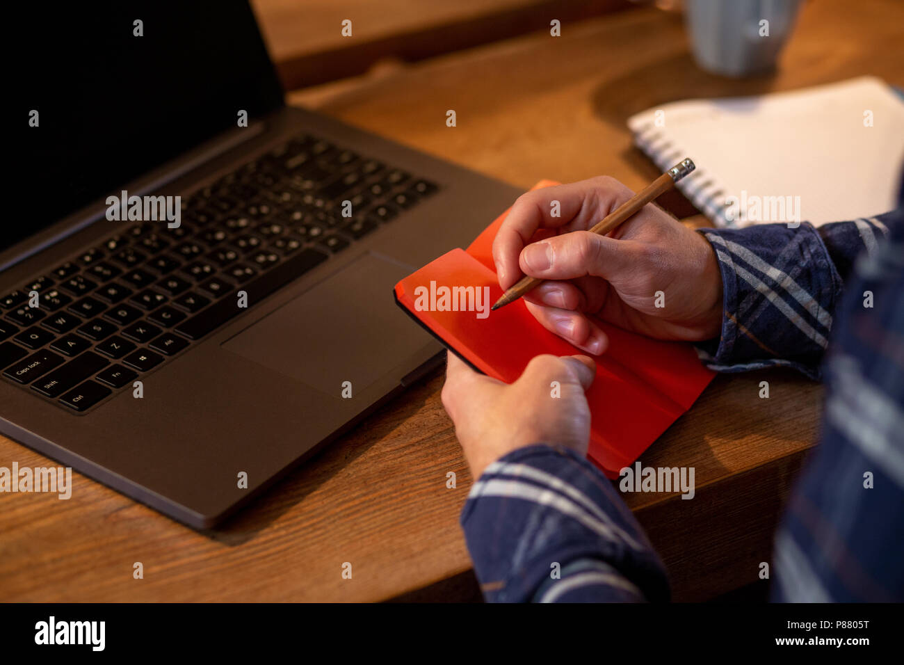 Cropped image of casual business man or freelancer planning his work on notebook, working on laptop computer with smart phone, cup of coffee on table at coffee shop or home office. Stock Photo