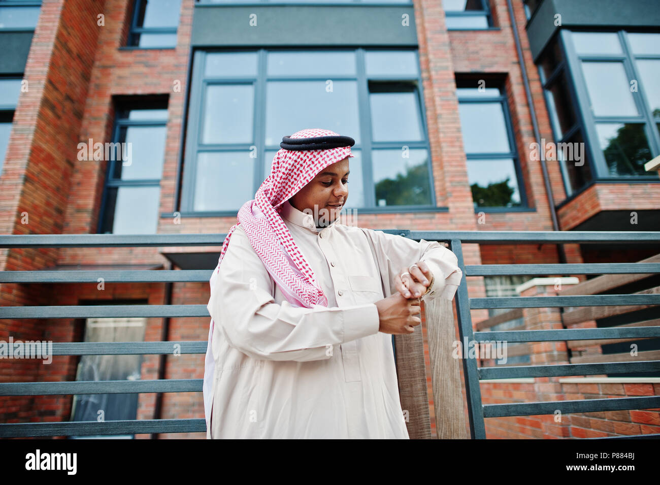 Middle Eastern arab man posed on street against modern building looking at his golden watches. Stock Photo