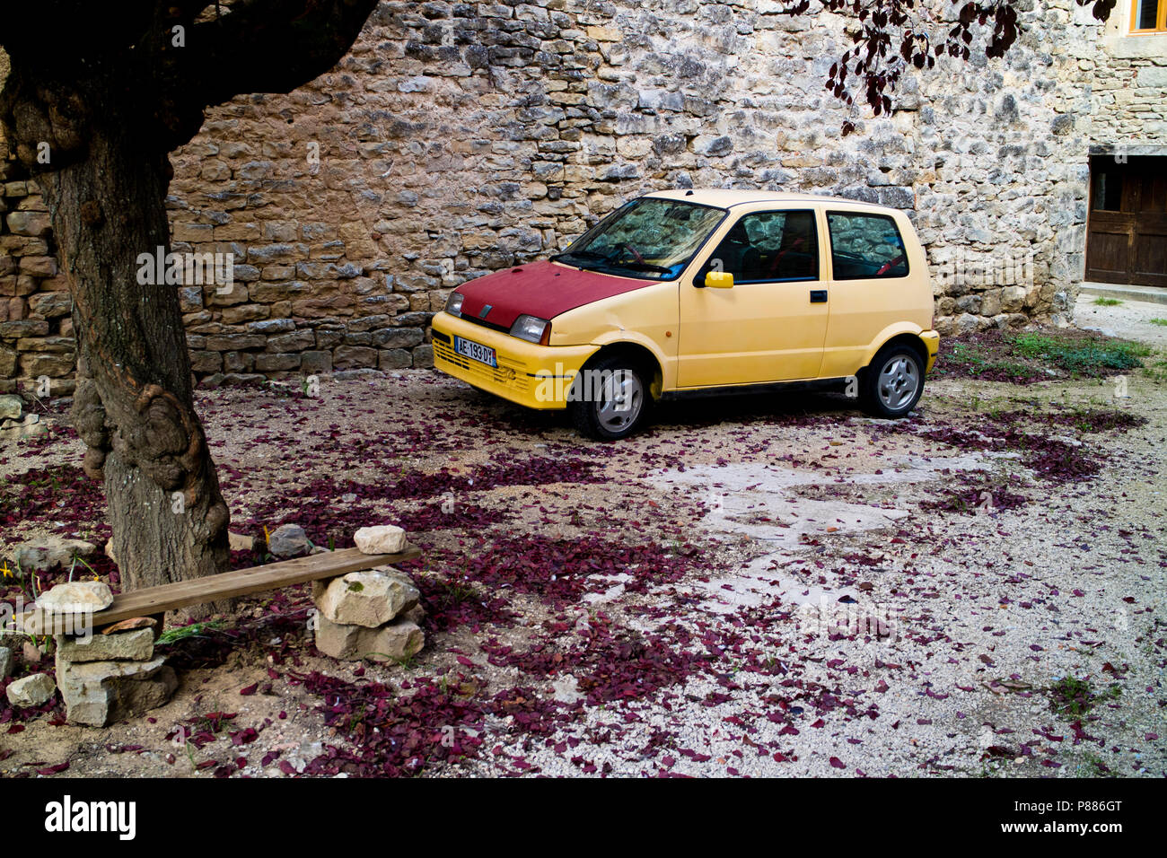 Older model Fiat Cinquecento car surrounded by red leaves in the churchyard in Arnac, part of the commune of Varen, Tarn et Garonne, Occitanie, France Stock Photo