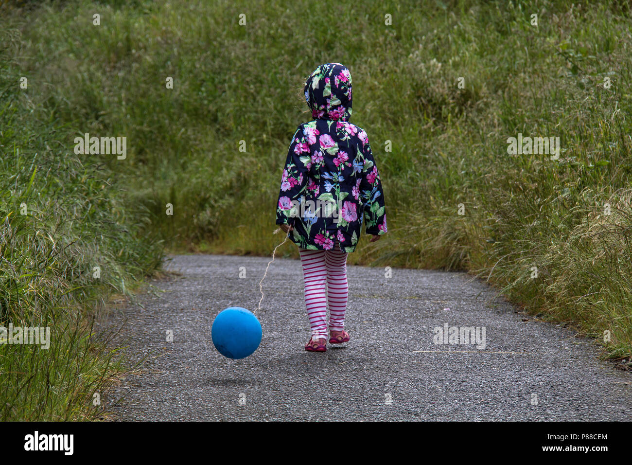 Girl in a bright colourful coat walks along a path with balloon on a cloudy and gloomy day. Stock Photo