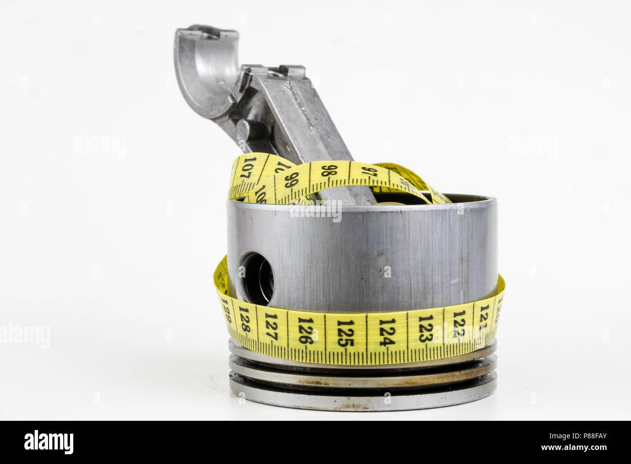 A piston from an internal combustion engine and a tailor measure on a white table. Car parts and tailor centimeter. White background. Stock Photo