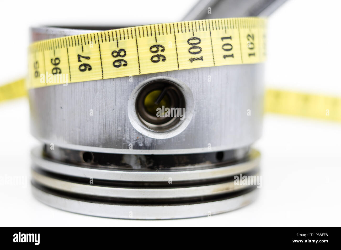 A piston from an internal combustion engine and a tailor measure on a white table. Car parts and tailor centimeter. White background. Stock Photo
