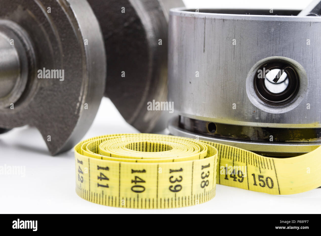 A piston from an internal combustion engine and a tailor measure on a white table. Car parts and