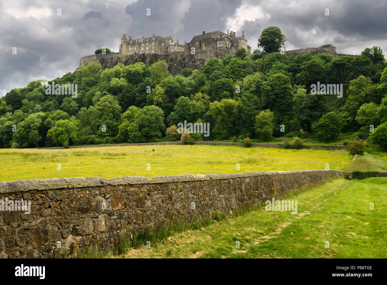 Stirling Castle on the cliff at Castle Hill in Stirling Scotland with stone wall of sheep pasture with dark clouds Stock Photo