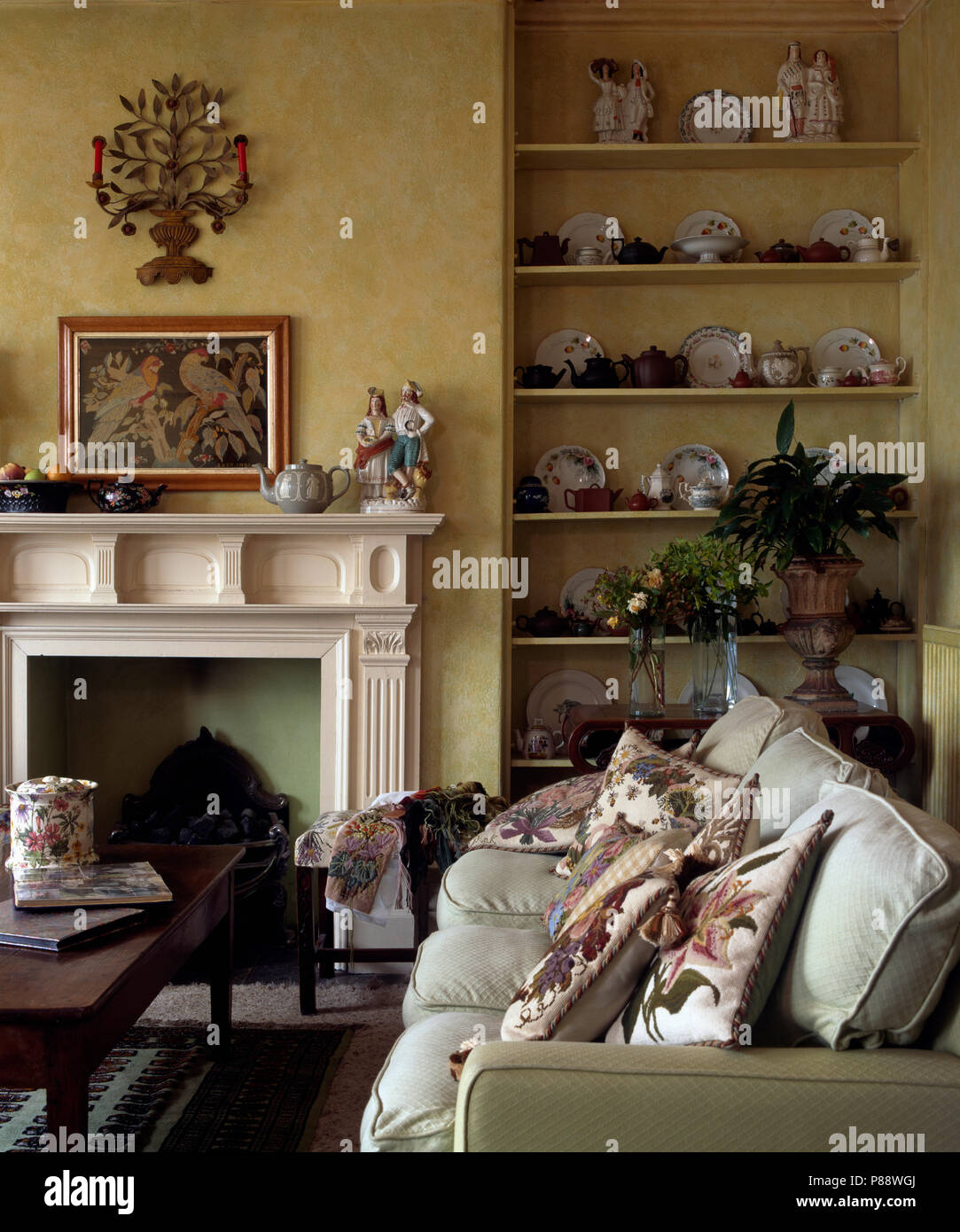 Decorative scone and tapestry picture above fireplace in country living room with sofa piled with tapestry cushions Stock Photo Alamy