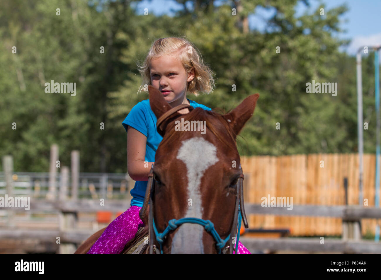 Young blonde girl, riding horse, looks directly in camera, smiling