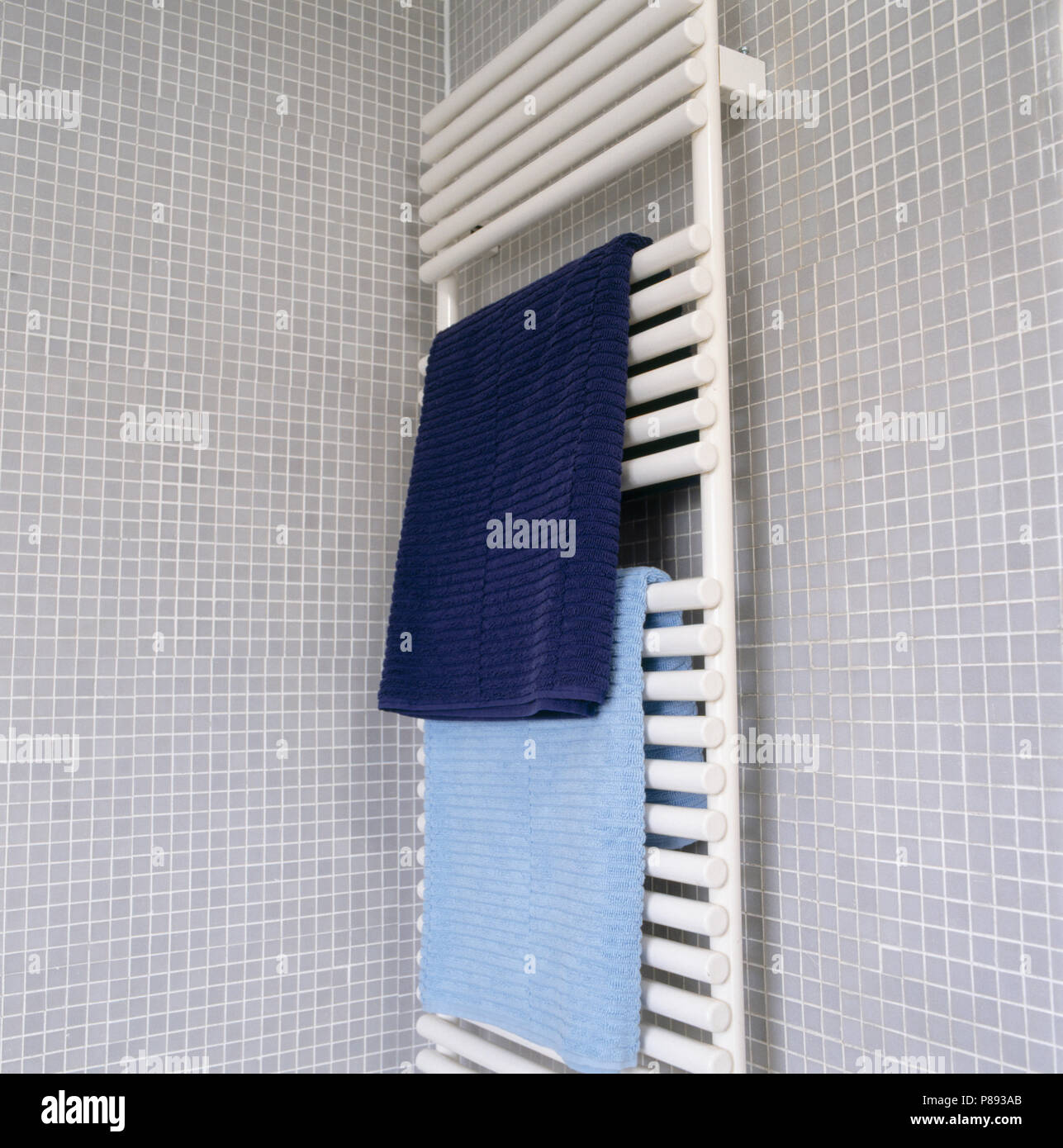 Blue towels on white heated towel rail on grey mosaic tiled bathroom wall Stock Photo Alamy