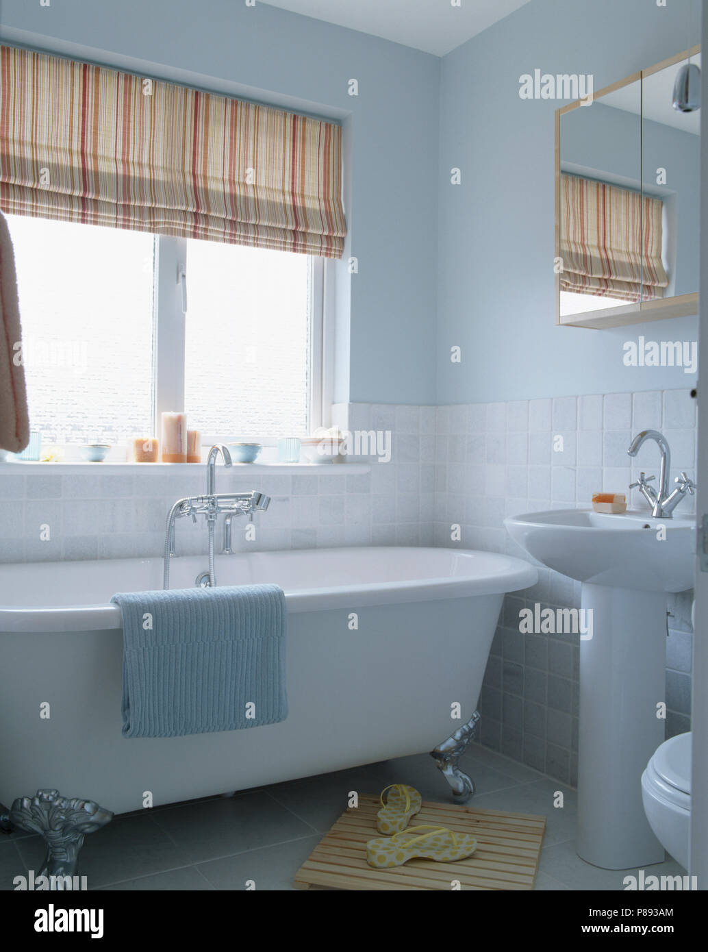 Neutral striped blind above white bath in pastel blue modern bathroom ...
