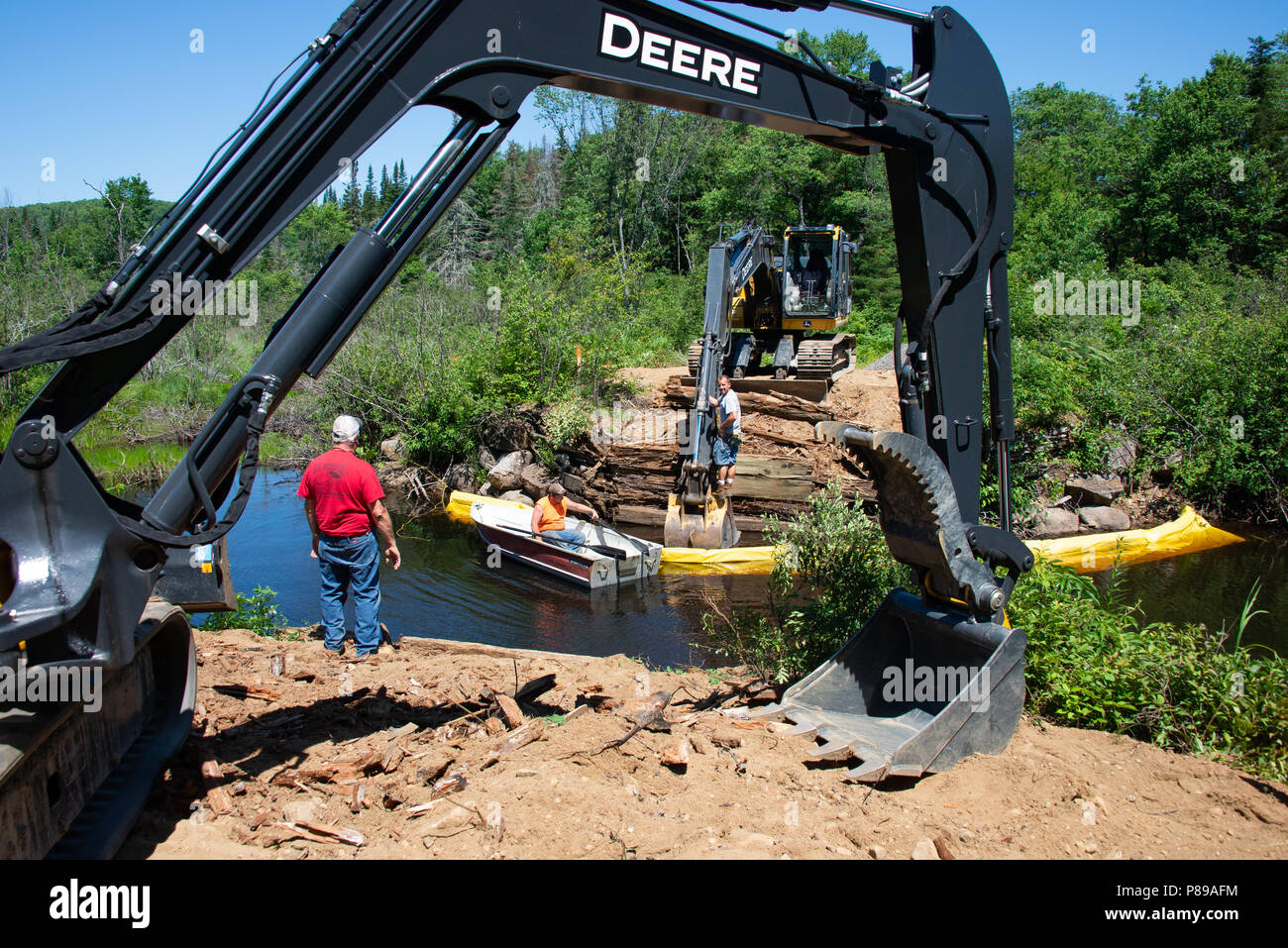 Two track hoe machines and three workers building a new logging bridge